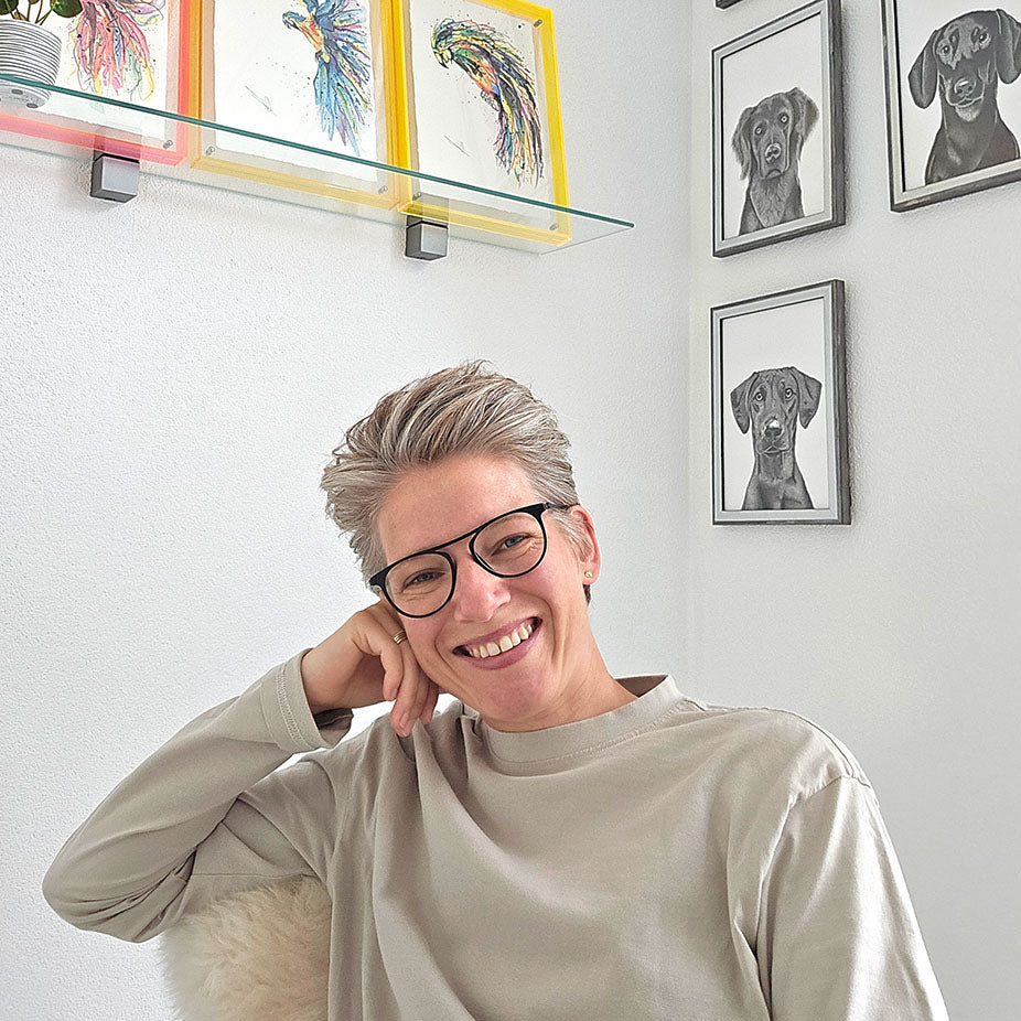 Quirine lacht naar de camera in atelier met op de achtergrond originele kunstwerken aan de muur