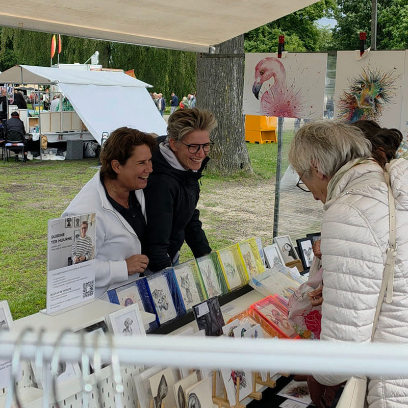 Quirine en Mirthe lachen vanachter de marktkraam in contact met klanten